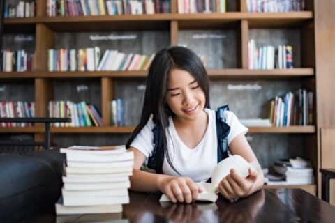 Young woman reading book sitting indoor in urban cafe.