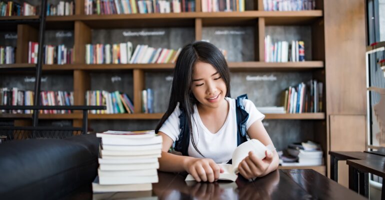 Young woman reading book sitting indoor in urban cafe.